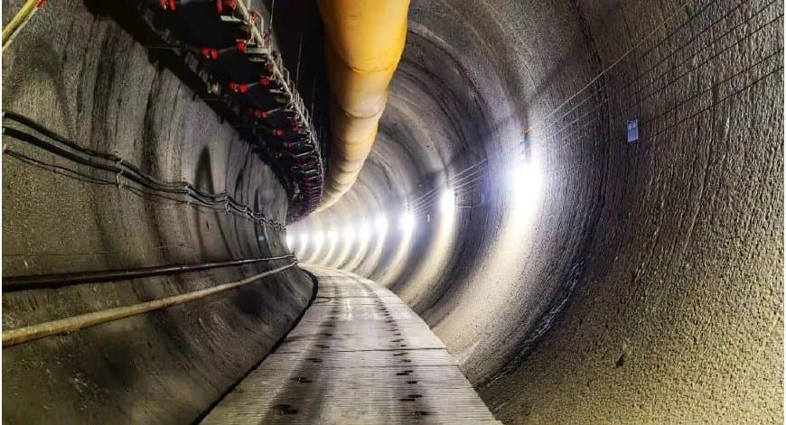 In-tunnel view along the bored hard-rock spiral with rock-bolted granitic walls, ventilation duct and services running back from the working face