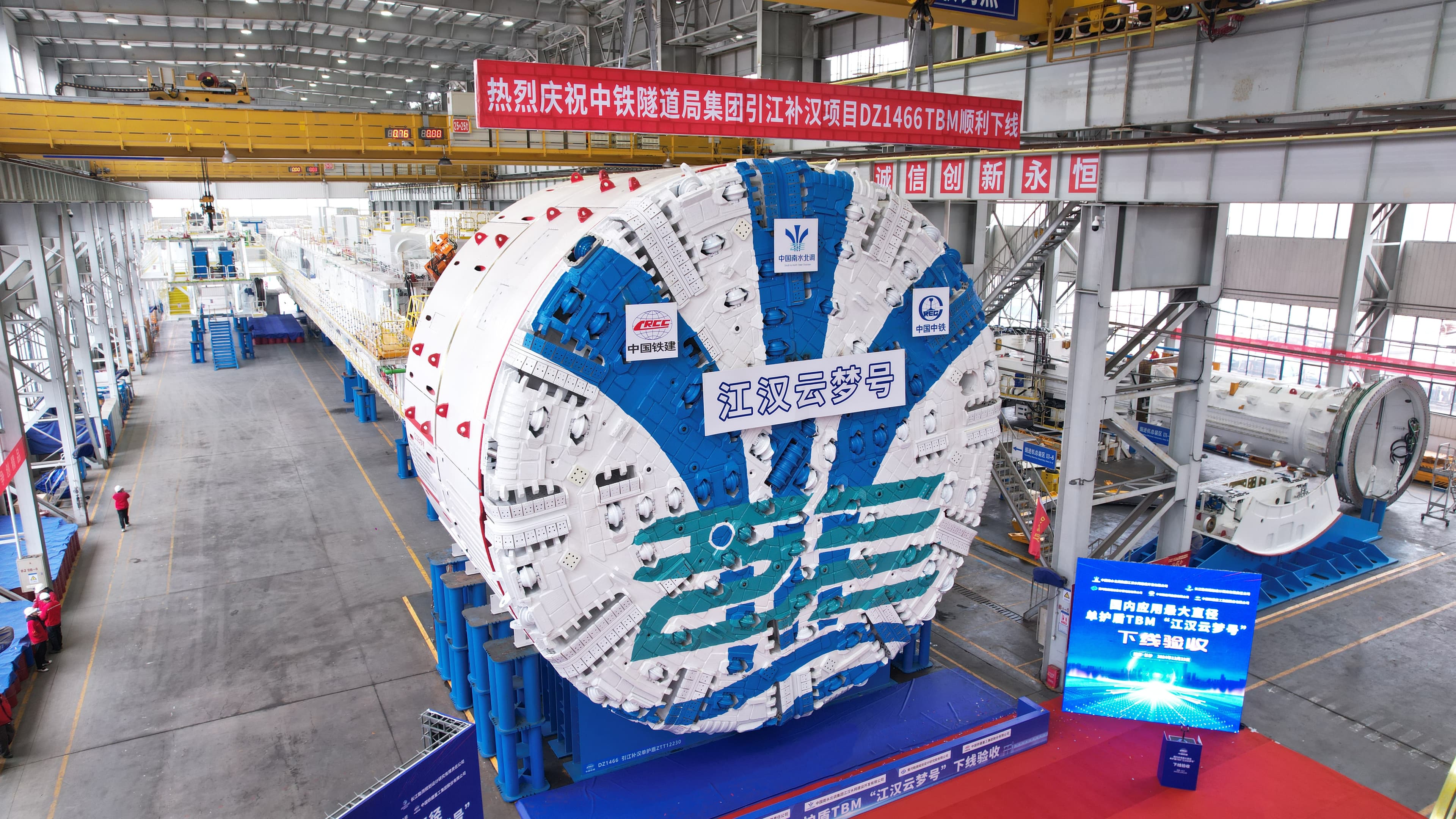 Jianghan Yunmeng 12.23 m single-shield TBM cutterhead in the factory hall with the "江汉云梦号" banner across the face and overhead bridge cranes above